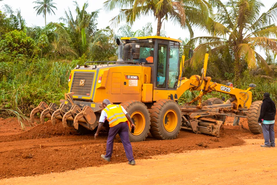 Motor grader shaping a laterite road while site staff supervise