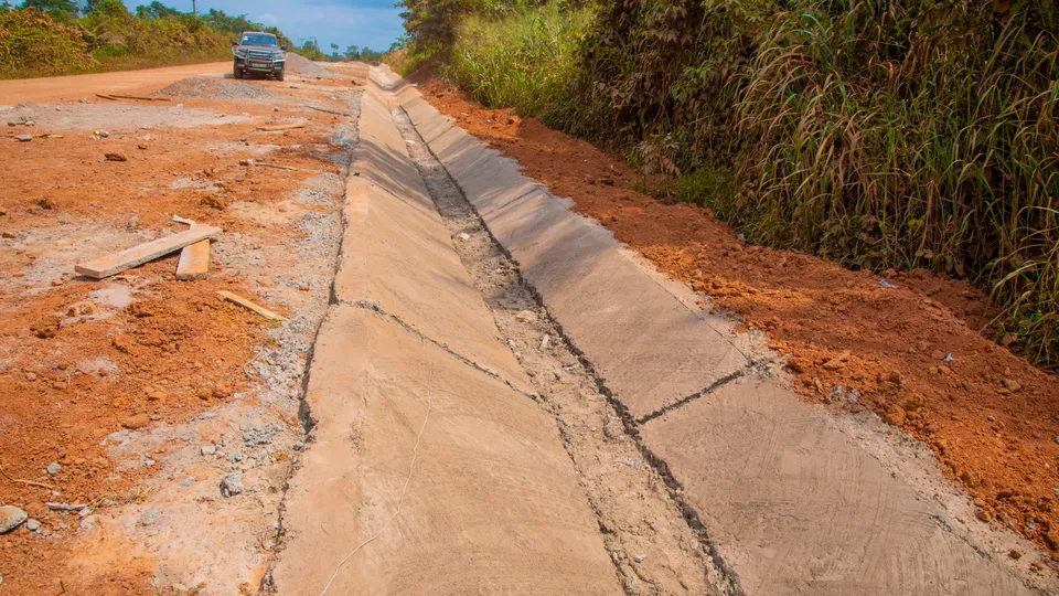 Completed concrete U-drain running alongside a gravel road