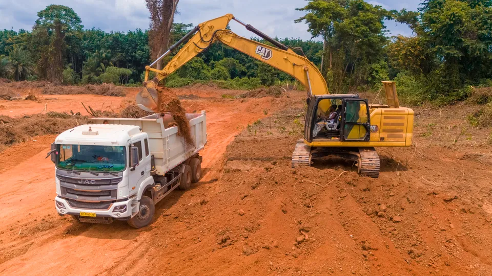Excavator loading red laterite into a white tipper truck on an earthworks site