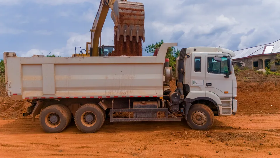 Excavator bucket above a white tipper truck being loaded with soil